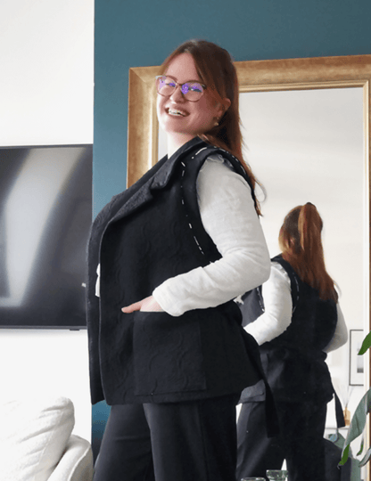 Femme souriante portant une veste Bogota noire, montrant son style décontracté et élégant dans un intérieur moderne.