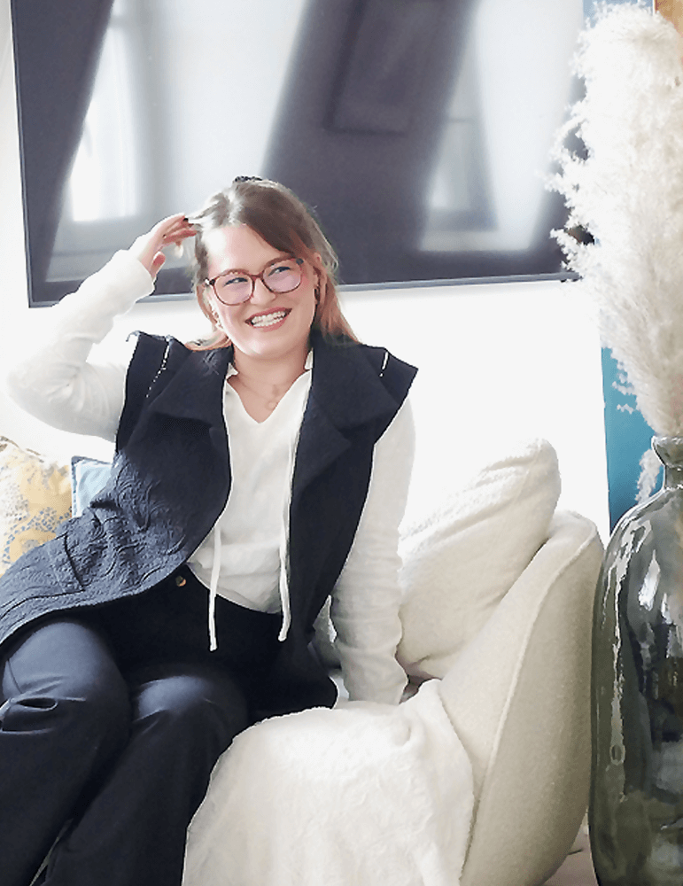 Femme souriante portant la veste Bogota, confortablement assise dans un intérieur élégant, mettant en valeur la couture et le style.
