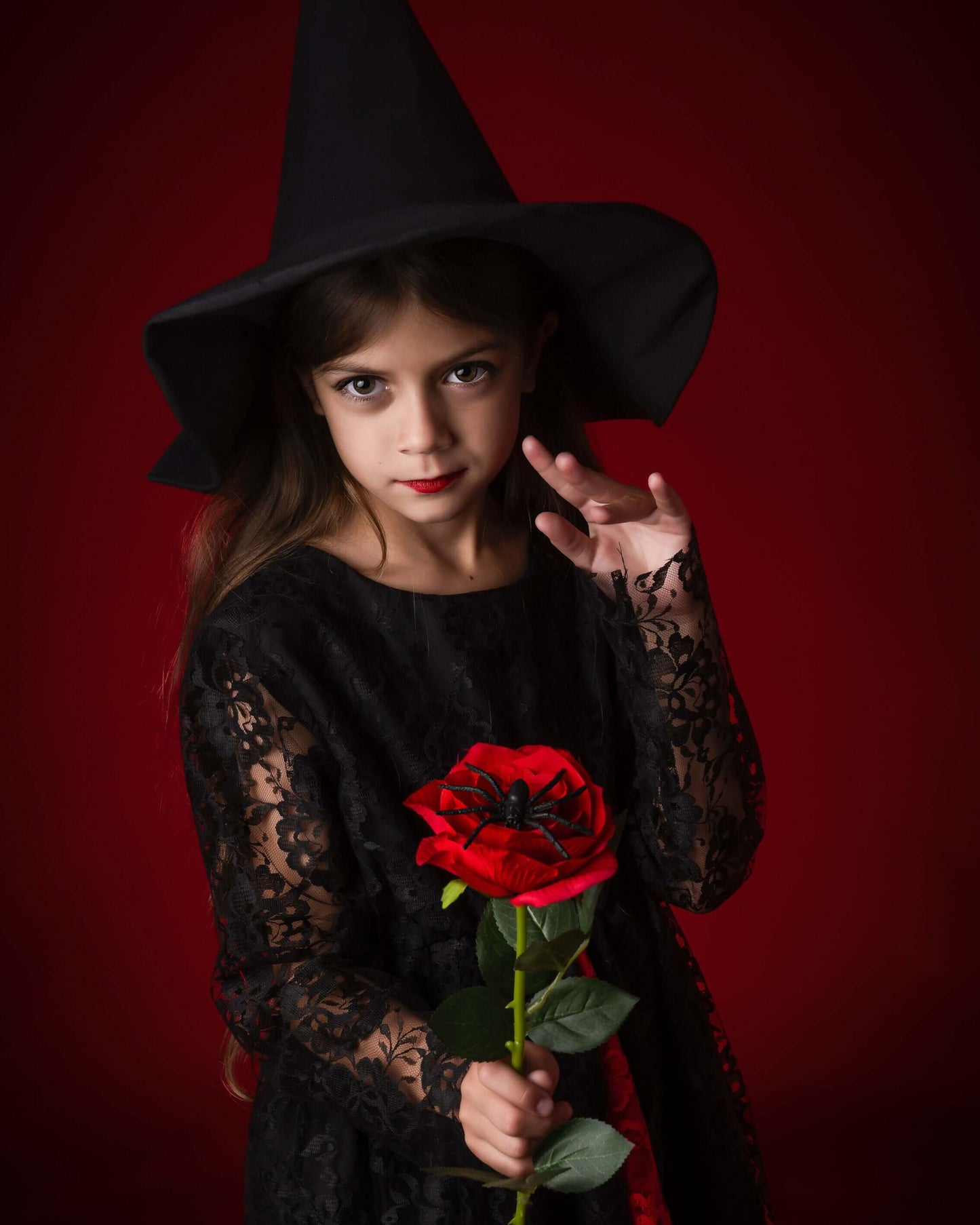 Petite fille en costume de sorcière avec un chapeau noir et une rose rouge, parfaite pour Halloween.