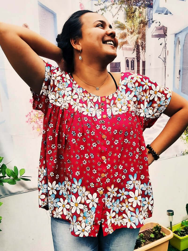 Femme souriante portant une blouse froncée rouge avec fleurs, idéale pour un style décontracté.