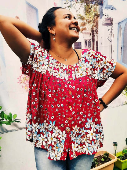 Femme souriante portant une blouse froncée rouge avec fleurs, idéale pour un style décontracté.