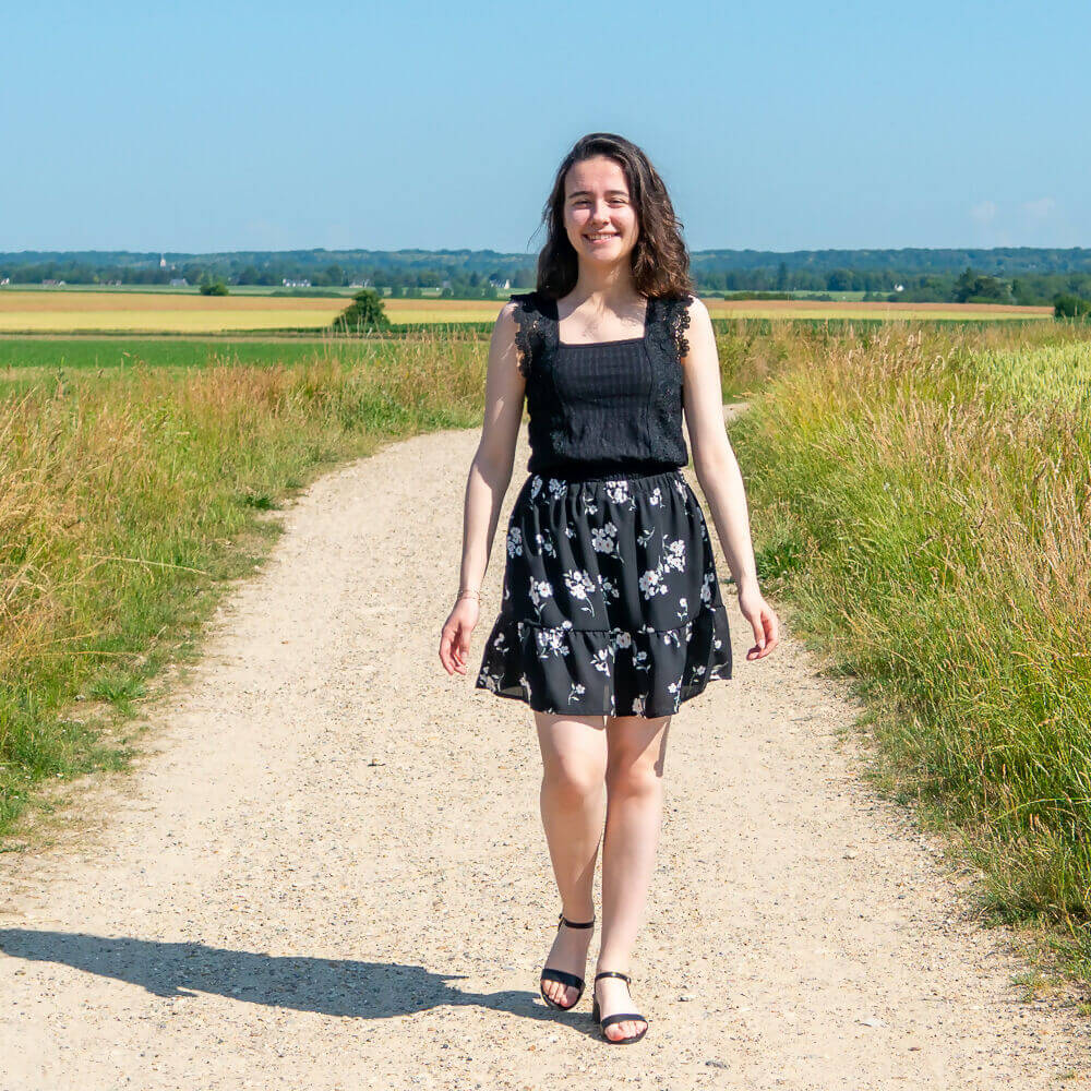 Femme marchant sur un chemin ensoleillé, portant une jupe noire à fleurs et un top noir, montrant un style bohème.