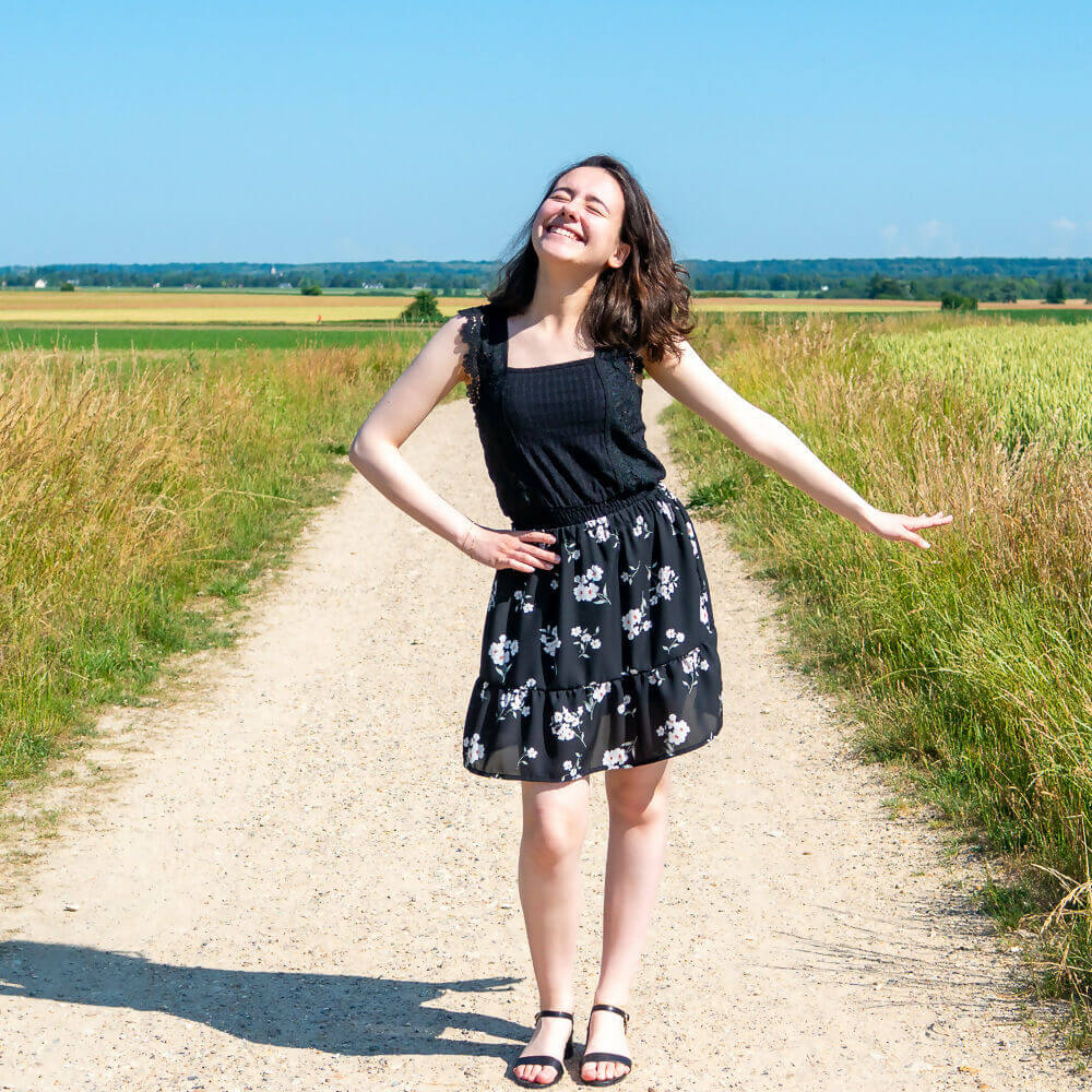 Jeune femme joyeuse portant une jupe bohème Mirabelle sur un sentier ensoleillé, entourée de nature.