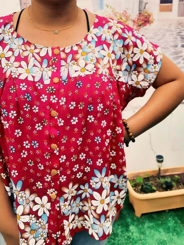 Femme portant une blouse ample à motifs floraux colorés sur fond rouge, style décontracté et élégant.