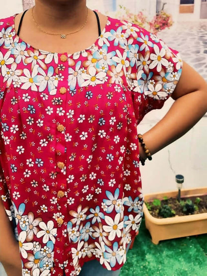 Femme portant une blouse ample à motifs floraux colorés sur fond rouge, style décontracté et élégant.