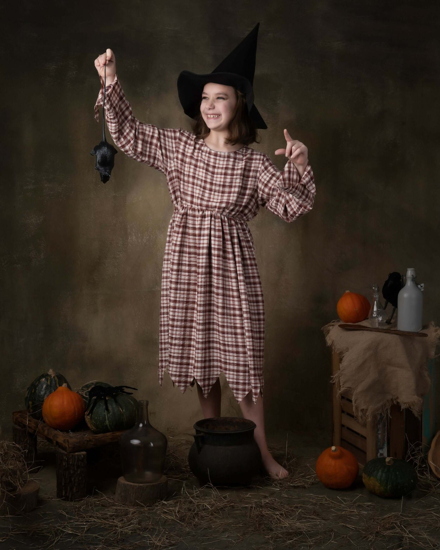 Fille en déguisement de sorcière avec chapeau, posant avec un rat en plastique, décor d'Halloween.