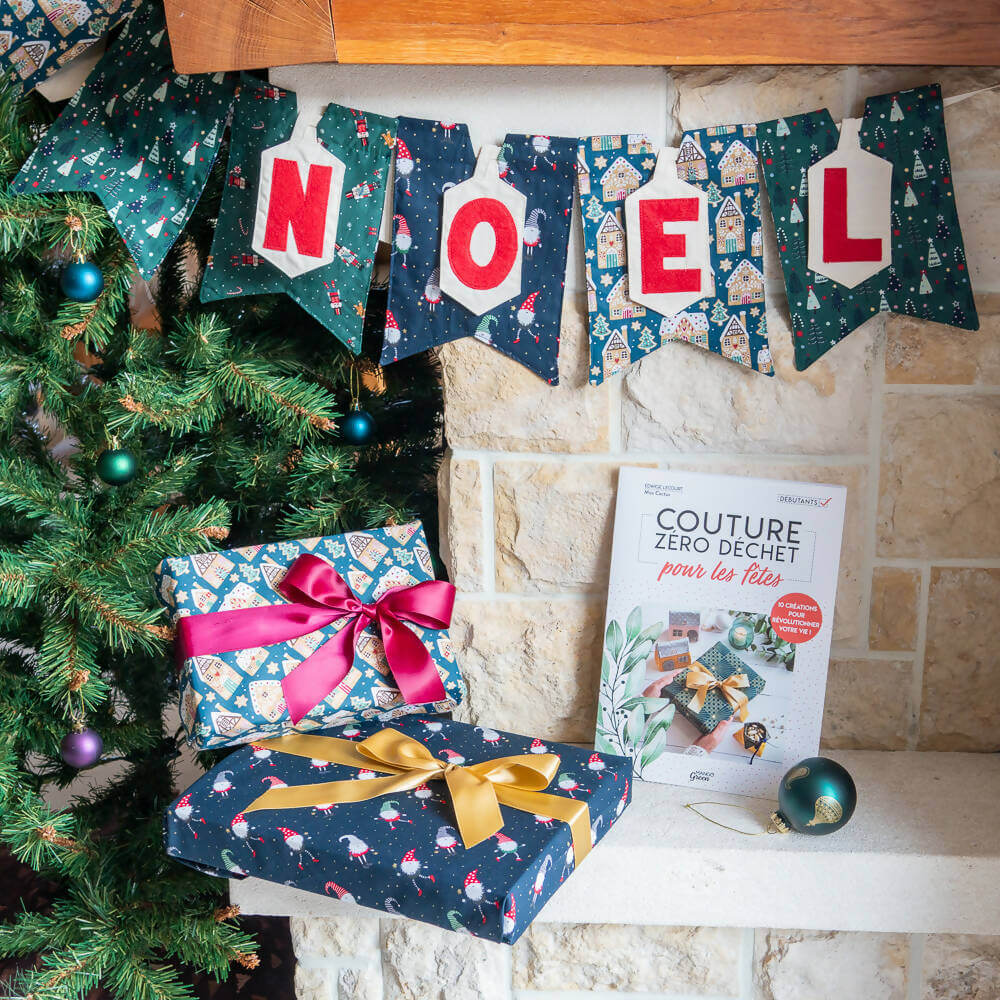 Guirlande en lettres appliquées "NOEL" décorant un coin festif avec des cadeaux et un livre de couture zéro déchet.