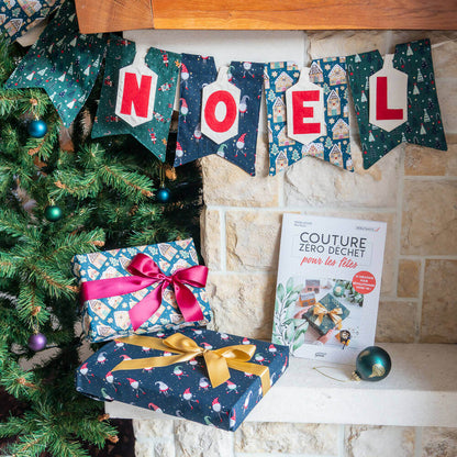 Guirlande en lettres appliquées "NOEL" décorant un coin festif avec des cadeaux et un livre de couture zéro déchet.
