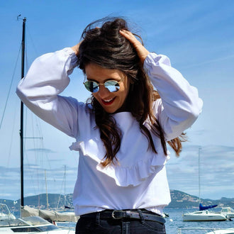 Femme portant la Blouse - Robe Embrun, un patron de couture pdf à télécharger, sur un port avec des voiliers en arrière-plan.