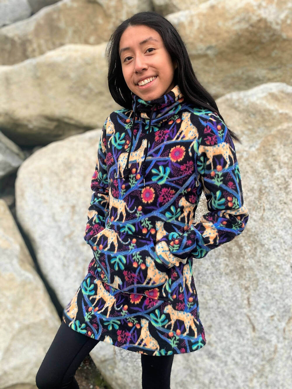 Jeune fille portant une robe colorée avec un col roulé, motif animal et floral, devant un paysage rocheux.