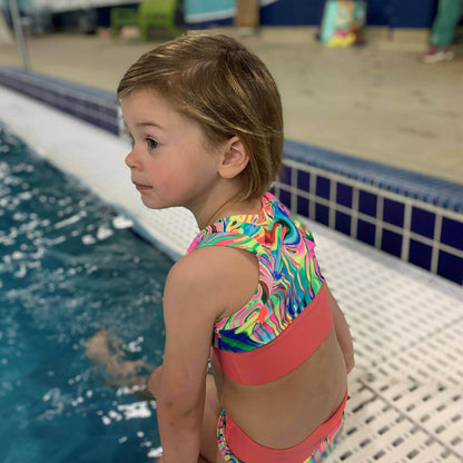 Enfant au bord d'une piscine portant un maillot de bain coloré, prêt à nager.