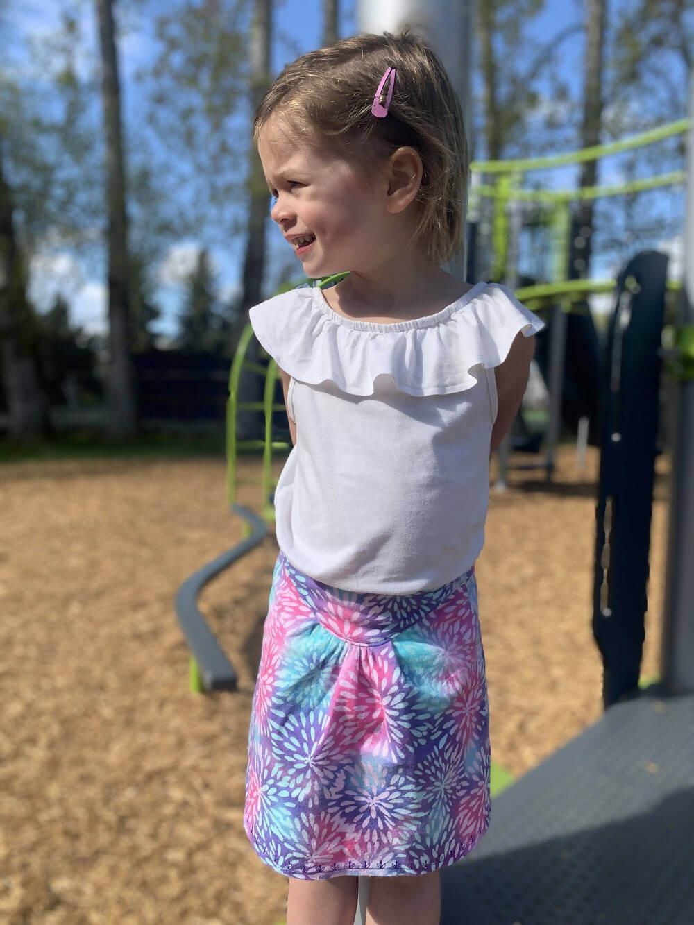 Fillette portant une jupe colorée et un haut à volants sur une aire de jeu.