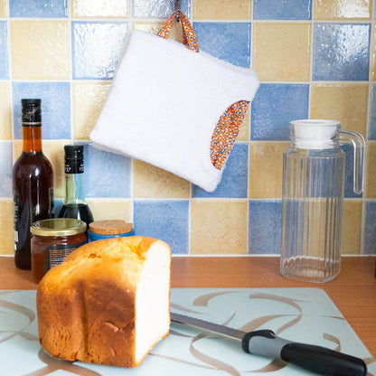 Essuie-tout biface lavable – Oups suspendu dans une cuisine, à côté d'un pain et couteau. Inclut patron de couture pdf à télécharger.