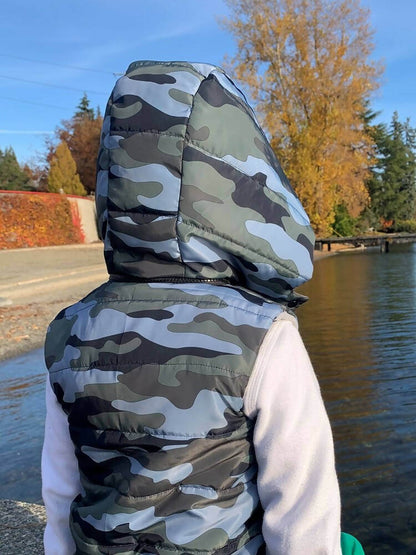 Enfant portant une Mini-KEZIA - Doudoune sans manches mixte pour enfants du 2 au 16 Ans, motif camouflage et capuche amovible.