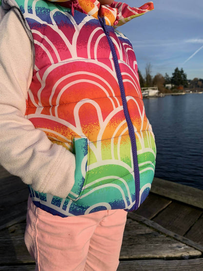 Enfant portant une Mini-KEZIA - Doudoune sans manches mixte pour enfants du 2 au 16 Ans colorée, sur un pont au bord d'un lac.