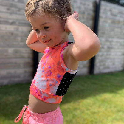 Enfant portant un Mini-ROXANA - Débardeur pour filles du 2 au 16 Ans, patron de couture pdf à télécharger, dans un jardin ensoleillé.