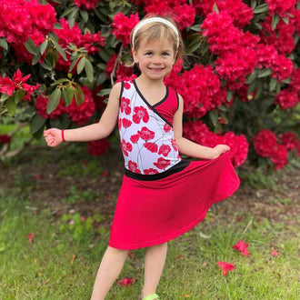 Fillette portant la Mini-SANDY - Robe cache-coeur pour filles du 2 au 16 Ans, devant un buisson fleuri. Patron de couture pdf à télécharger disponible.