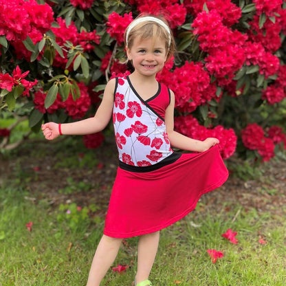 Fillette portant la Mini-SANDY - Robe cache-coeur pour filles du 2 au 16 Ans, devant un buisson fleuri. Patron de couture pdf à télécharger disponible.