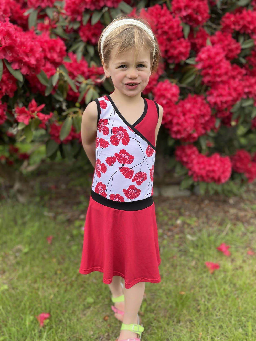 Fille portant la robe Mini-SANDY - Robe cache-coeur pour filles du 2 au 16 Ans, patron de couture pdf à télécharger, devant des fleurs rouges.