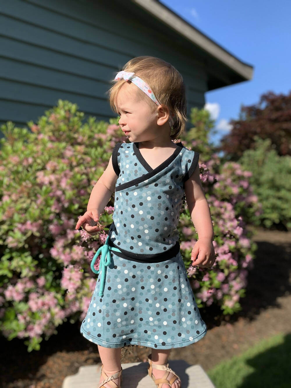 Fille portant Mini-SANDY - Robe cache-coeur pour filles du 2 au 16 Ans, patron de couture pdf à télécharger, en extérieur avec fleurs.