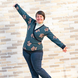 Pull sweat croisé, 34 au 56, 4 statures – Cannelle, patron de couture pdf à télécharger. Femme portant le pull devant un mur en briques.