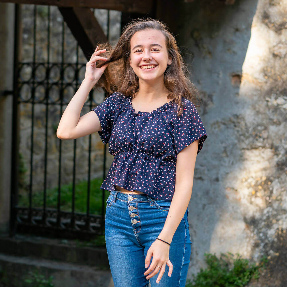 Jeune femme souriante en haut à motifs devant une porte en pierre