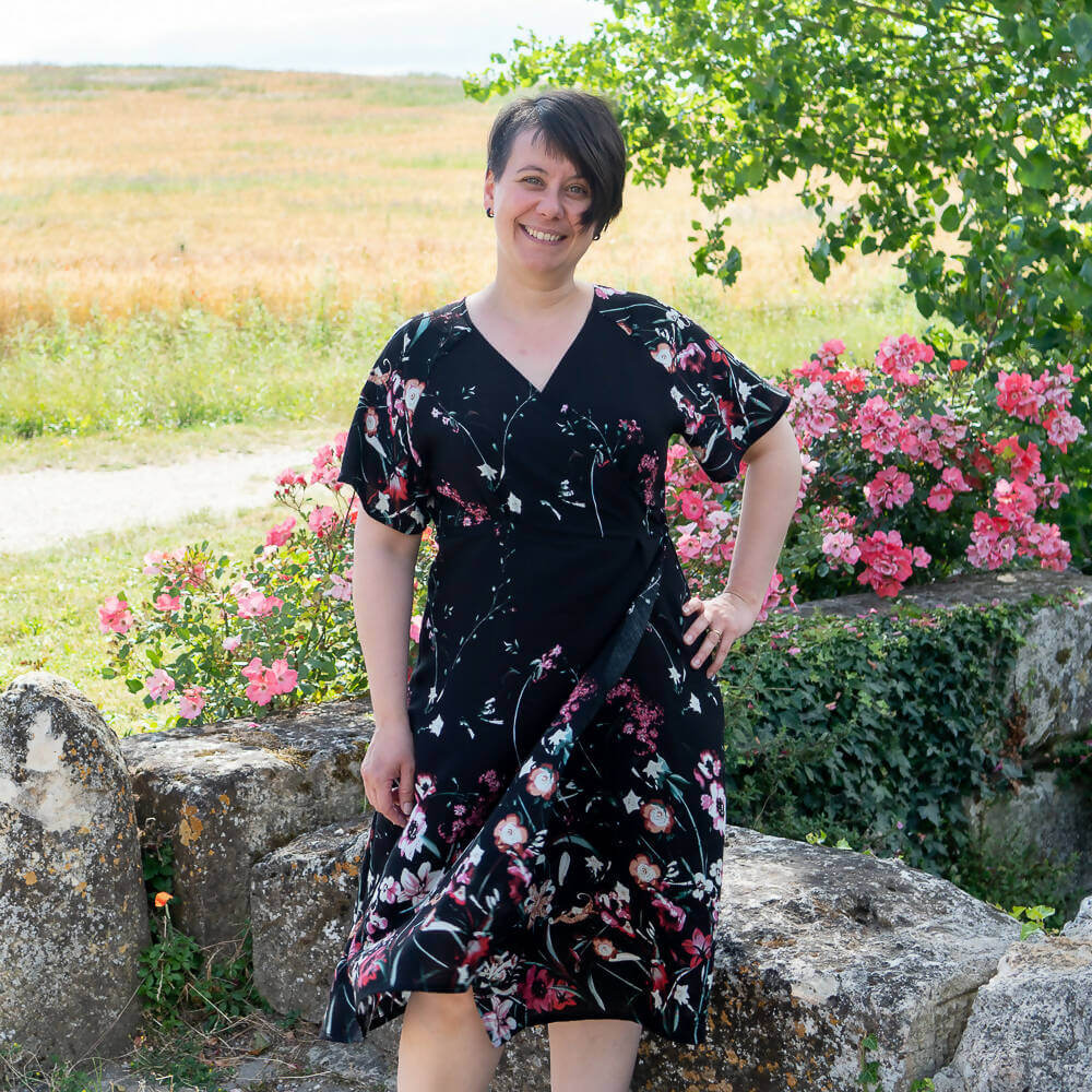 Robe blouse portefeuille, 34 au 56, 4 statures – Sésame, patron de couture pdf à télécharger, portée en extérieur avec des fleurs en arrière-plan.