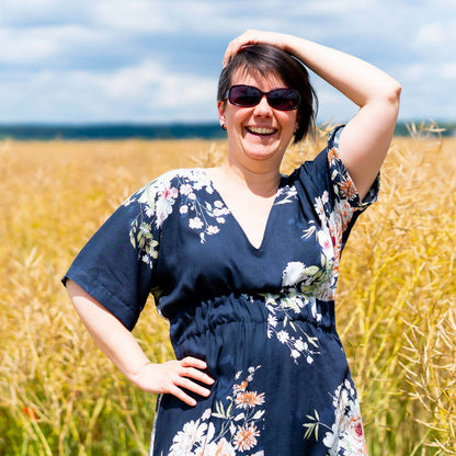 Femme souriante portant la Robe longue, 34 au 52, 4 statures, patron débutant – Wasabi dans un champ, style kimono et motif floral.