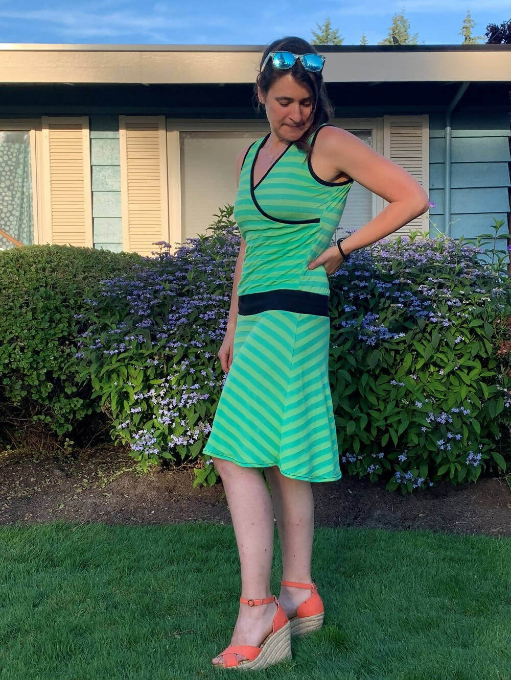 Femme portant SANDY - La robe cache-coeur pour femmes du 34 au 54, verte à rayures, avec jupe évasée au genou dans le jardin.