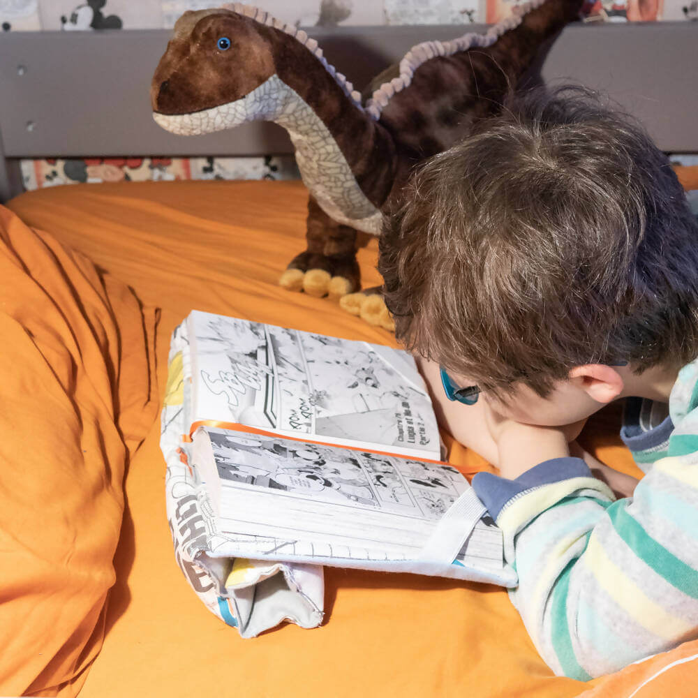 Enfant utilisant le Support à livre – Lexie avec patron de couture pdf à télécharger, peluche dinosaure en arrière-plan.