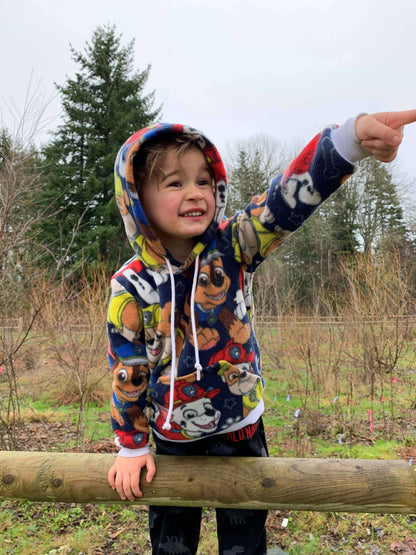 Enfant souriant portant un sweat à capuche coloré, pointant vers l'horizon lors d'une promenade en plein air.